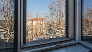 Une fenêtre donnant sur un bâtiment avec un toit rouge, des voitures garées et des arbres sans feuilles.