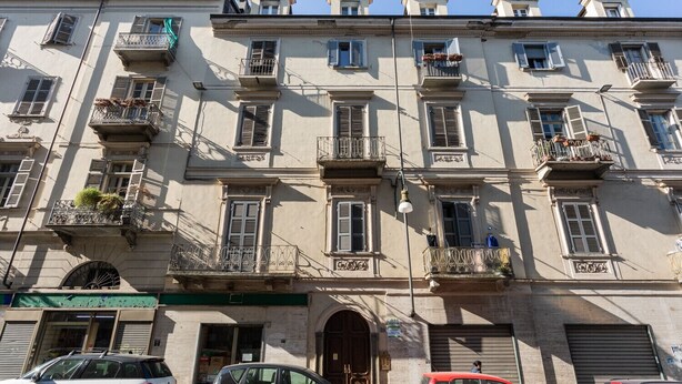 Un immeuble à plusieurs étages doté de balcons, avec une entrée au niveau du sol et des voitures garées.