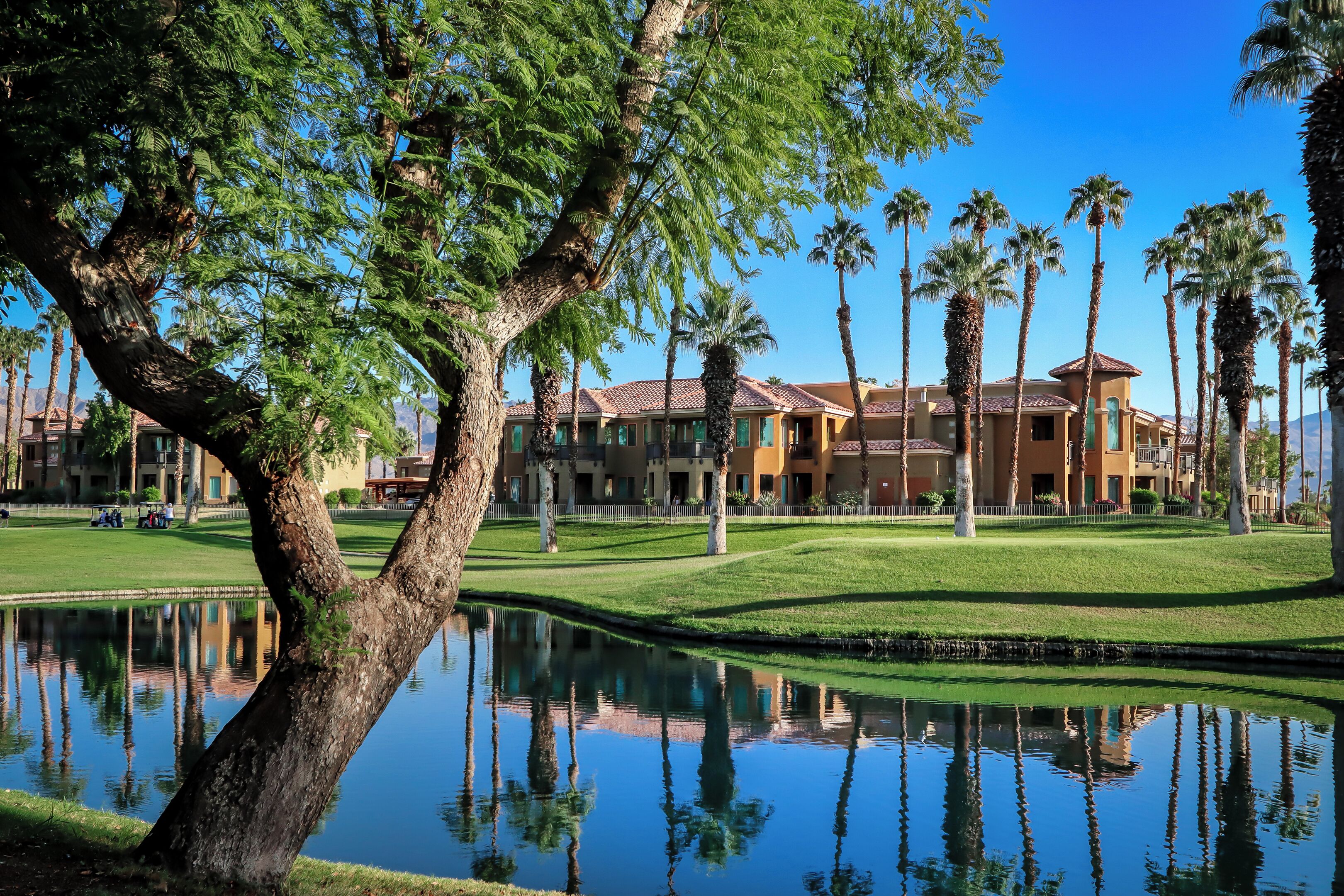 Un campo de golf con un estanque, palmeras y un edificio con techo de tejas.
