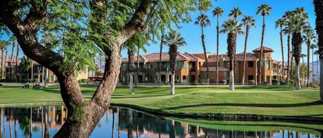 Un campo de golf con un estanque, palmeras y un edificio con techo de tejas.