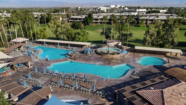A resort with multiple swimming pools, sun loungers, and a golf course in the background.