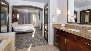 A modern hotel room with a large bed, a bathroom with a granite countertop, and a large mirror.