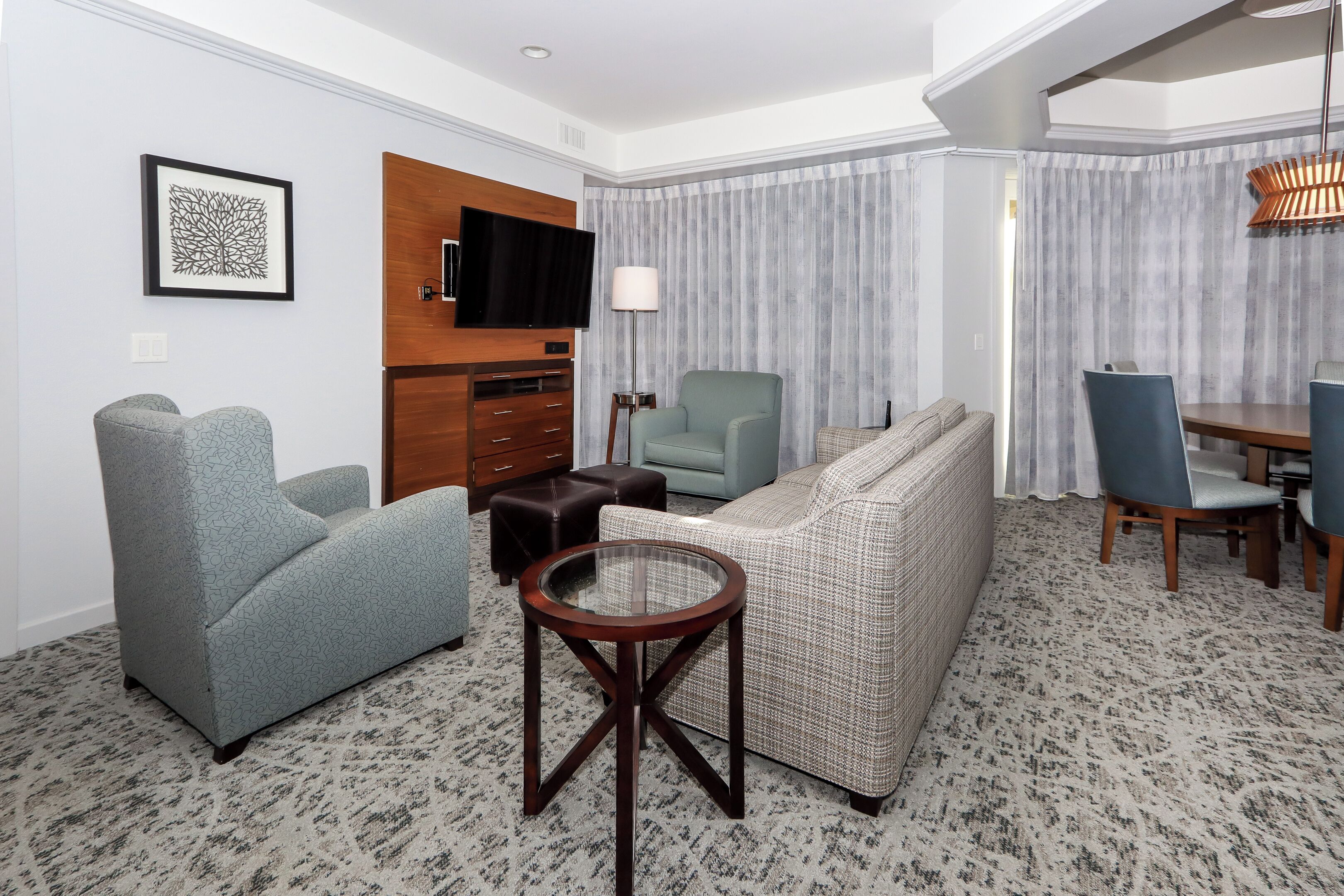 Una sala moderna con un sofá, sillones, una mesa de centro de cristal, un televisor de pantalla plana, una lámpara y un comedor con sillas y una mesa.