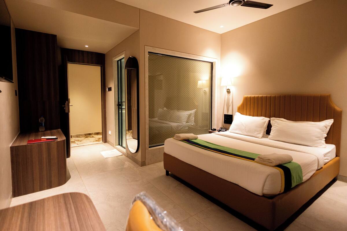 A hotel room with a bed, a desk, a mirror, and a door leading to a bathroom.