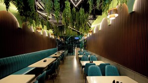 A restaurant with booths and tables, a wooden wall, hanging plants, and pendant lights. - HOTEL GOLDEN TULIPZ (Mumbai)