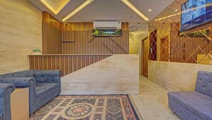 A hotel reception area with a modern design, featuring a reception desk, two sofas, a patterned rug, and a large TV screen. - HOTEL GOLDEN TULIPZ (Mumbai)