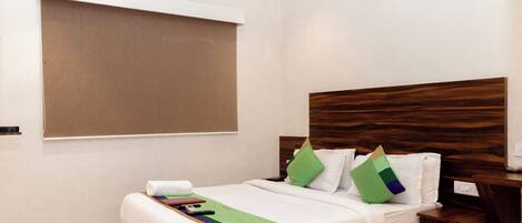 Habitación de hotel con cama, mesita de noche, aire acondicionado de pared y ventana con persiana.