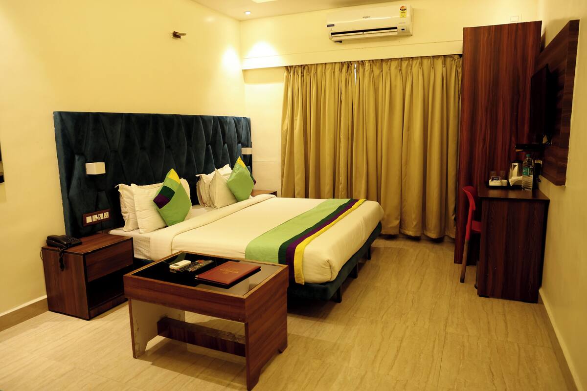 A hotel room with a bed, bedside table, nightstand, and a desk with a chair.
