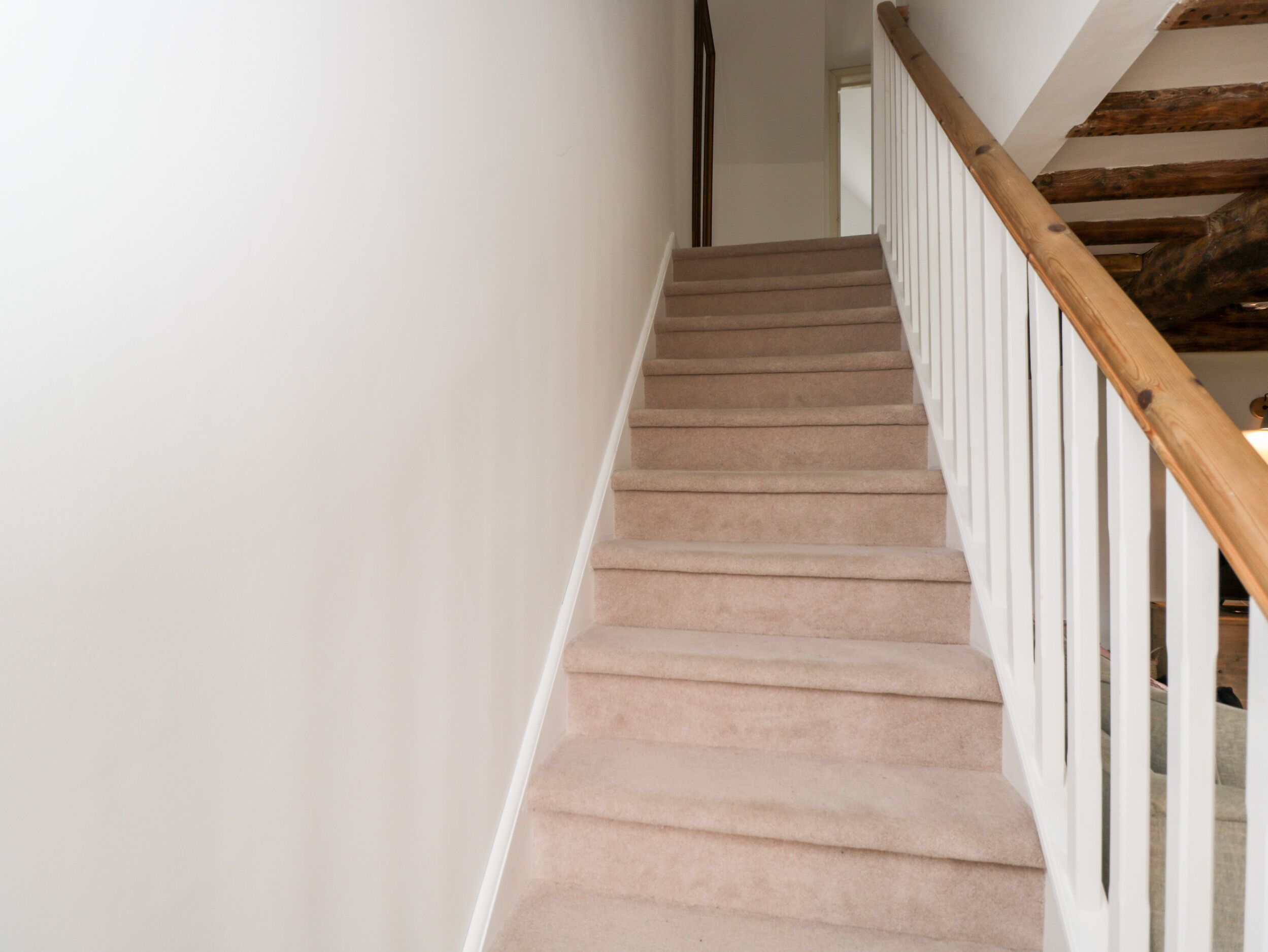 A staircase with beige carpet and white railings, leading to a room with a wooden ceiling beam.