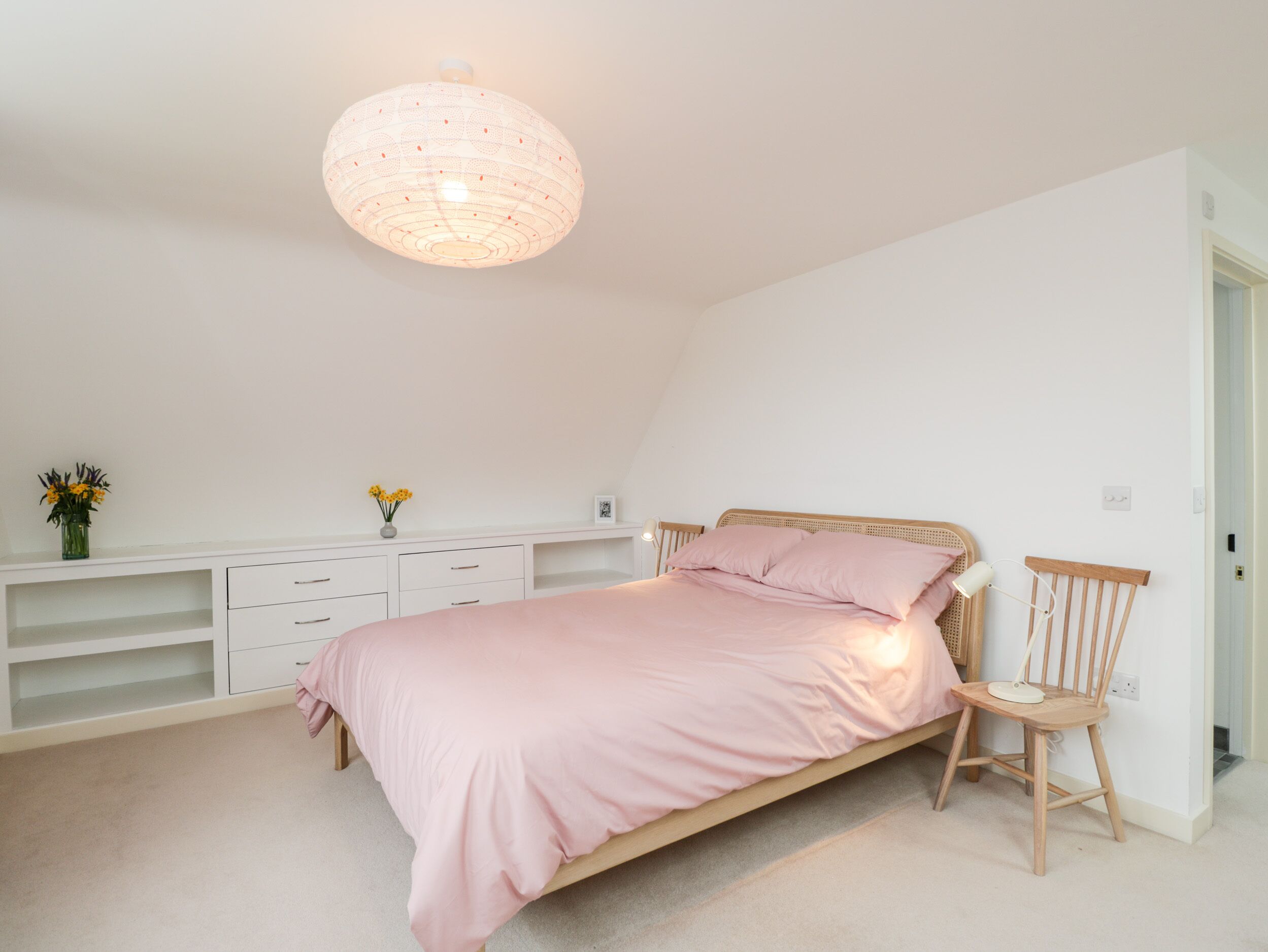 A bedroom with a single bed, a white dresser, a wooden chair, and a hanging light fixture.