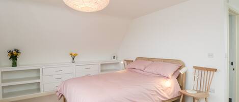 A bedroom with a single bed, a white dresser, a wooden chair, and a hanging light fixture.