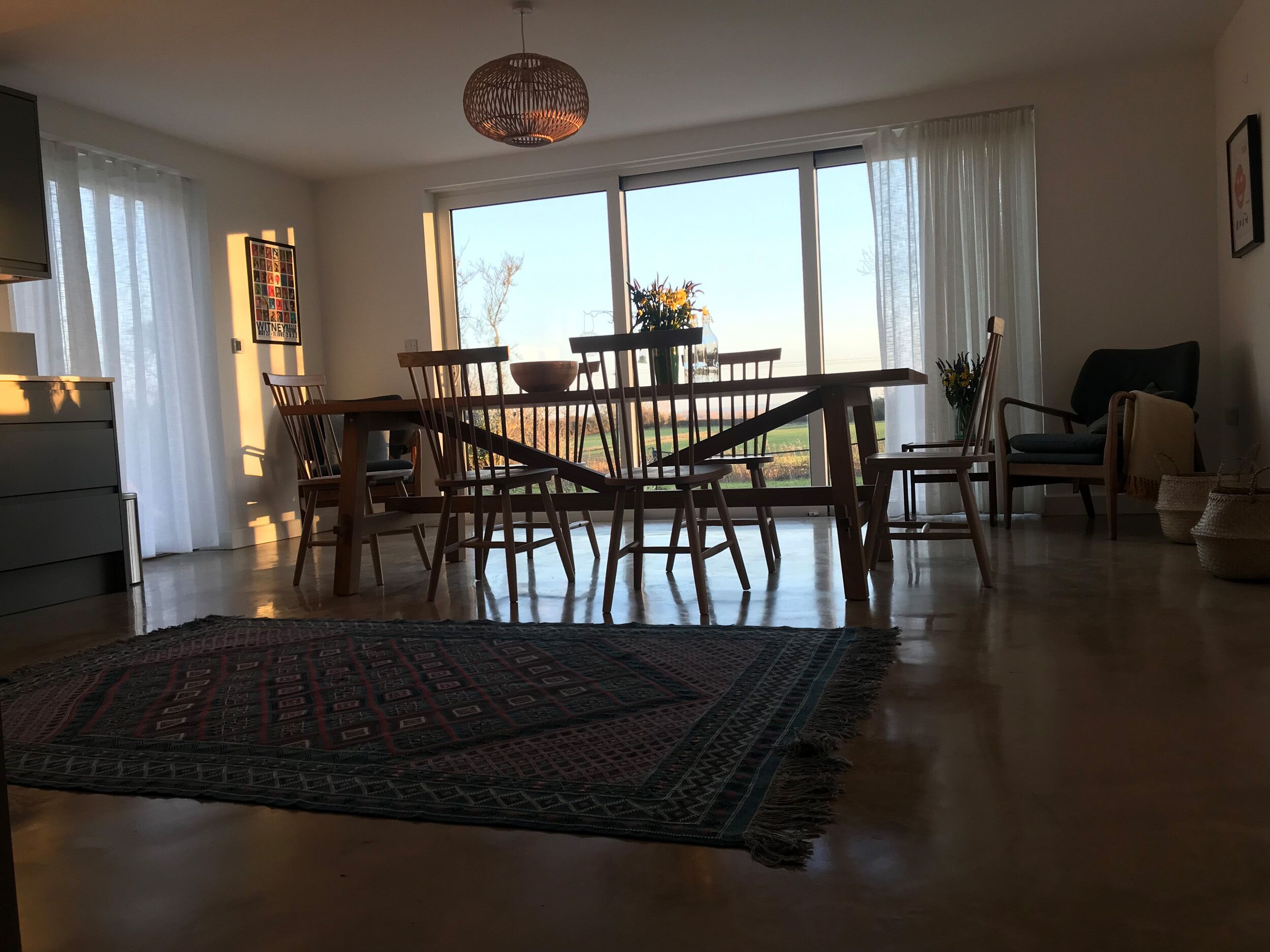 A spacious living room with a large window, a dining table, and a cozy rug.