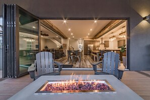 Ein Essbereich im Freien mit Feuerstelle, Holzterrasse und Blick ins moderne Wohnzimmer.