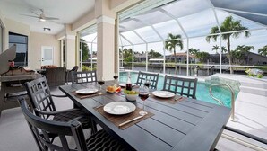 Un área de comedor al aire libre con vista a la piscina, que incluye una mesa para cuatro, sillas y una parrilla.