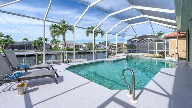 Zona de piscina con terraza cubierta, sillas de descanso y vistas al agua y edificios circundantes.