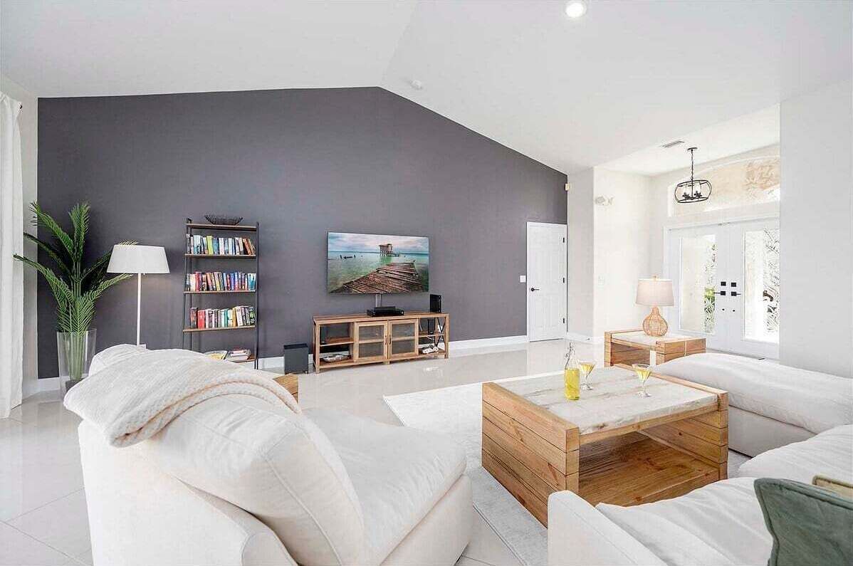 Ein modernes Wohnzimmer mit grauer Akzentwand, einem Holztisch, weißen Sofas, einem Bücherregal und einem Fernseher.