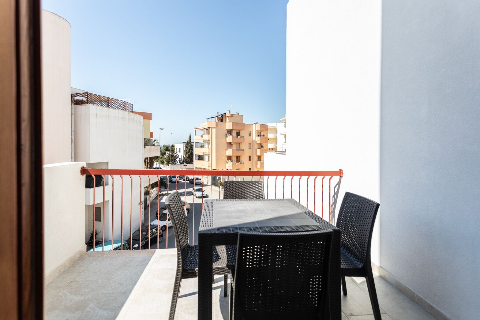 A balcony with a table and chairs, overlooking a street with buildings.