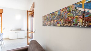 Un salon avec un canapé marron, un meuble blanc et une fresque colorée représentant une scène de rue.
