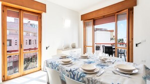 Un coin repas avec une table dressée pour quatre personnes, de grandes fenêtres et une vue sur les bâtiments environnants.
