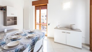 Un espace repas moderne avec une table dressée pour quatre personnes, un meuble blanc doté d’un plan de travail et une vue sur l’extérieur grâce à une porte vitrée.