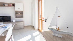 Une pièce moderne et bien éclairée, avec un bureau en bois, un téléviseur, une bibliothèque et une maquette de voilier accrochée au mur.