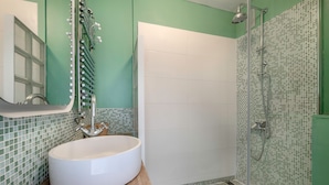 A bathroom with a large white sink, a mirror, and a shower with mosaic tiles.