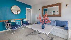 A modern living room with a blue accent wall, a round mirror, a white sofa, and a coffee table with a vase of flowers.