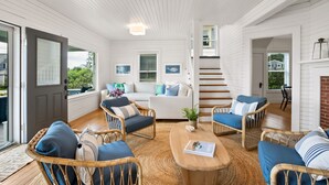 Une pièce spacieuse, meublée de meubles en osier, avec une table basse en bois et un escalier menant à un niveau supérieur.