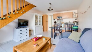 Een moderne woonkamer met een houten trap, een televisie, een eethoek met een tafel en stoelen, en een keuken met kasten en een magnetron.