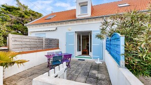 Een huis met een pannendak, een houten omheining en een klein terras met een tafel en stoelen.
