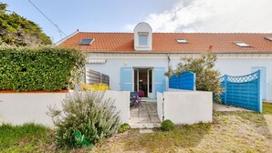 Een huis met een rode pannendak, een witte gevel en een blauwe deur.