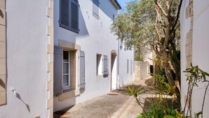 A narrow alleyway between buildings with white walls and shutters, a gravel path, and a tree with green foliage. - 150m from St Martin de Ré harbour, studio for 2 (Saint-Martin-de-Ré)