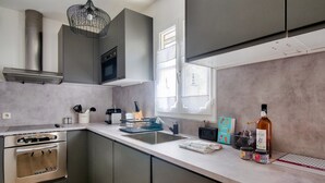 A modern kitchen with stainless steel appliances, grey cabinets, and a large window providing natural light. - 150m from St Martin de Ré harbour, studio for 2 (Saint-Martin-de-Ré)