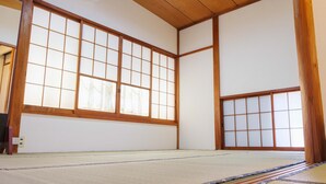 Ein Raum mit Tatami-Matten, großen Shoji-Schirmen, Holzbalken und traditioneller japanischer Gestaltung.