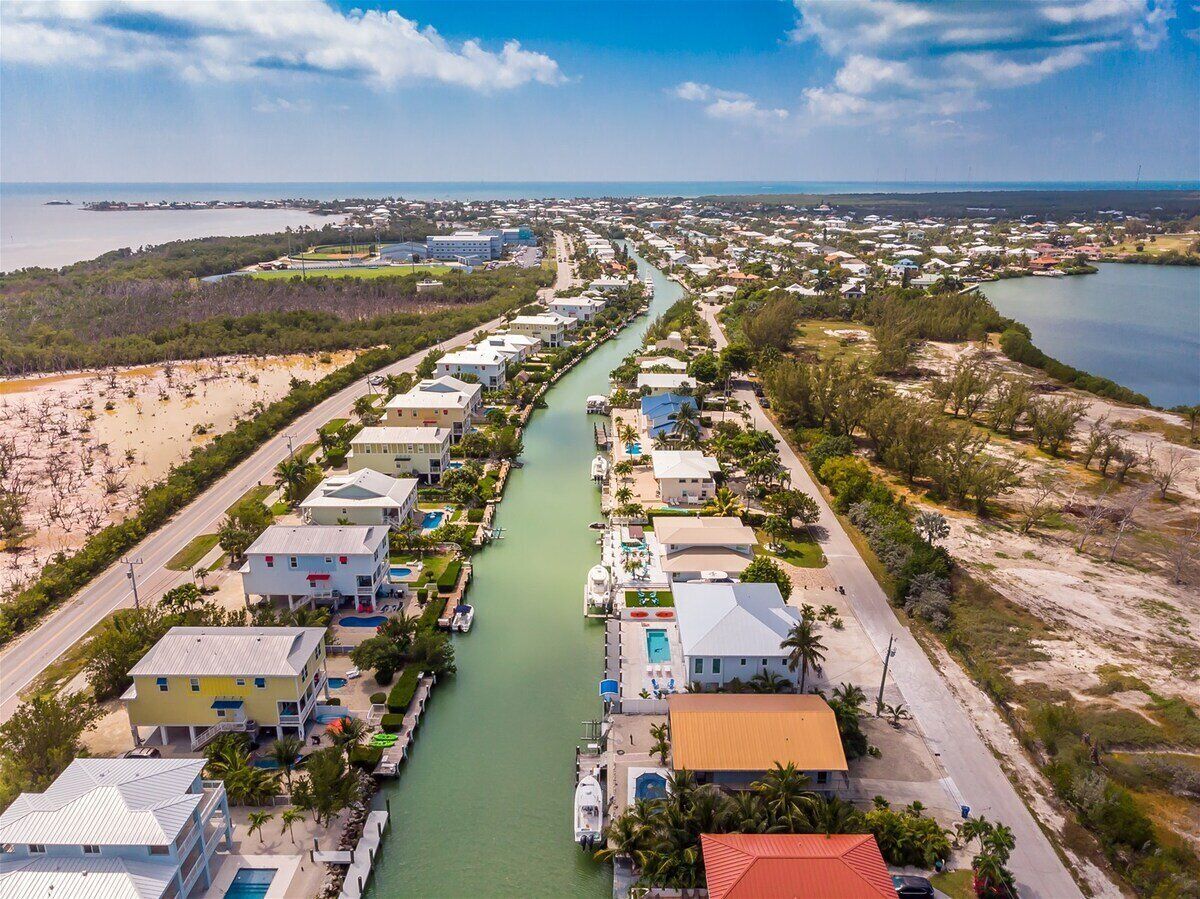 A coastal residential area with houses along a river, some with pools and beachfront access.