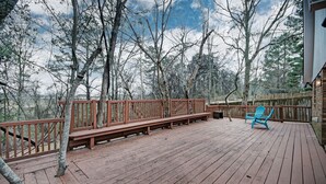 A wooden deck with a wooden bench and a blue chair, surrounded by trees.