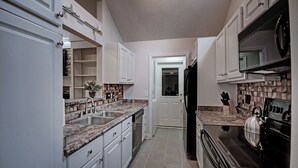 A kitchen with white cabinets, granite countertops, a black refrigerator, and a stove.