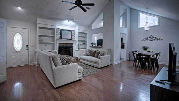A spacious living room with a fireplace, a dining area with a table and chairs, and a kitchen in the background.