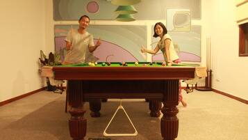 A pool table in a room with a large abstract painting on the wall, a hanging lamp, and a carpeted floor.