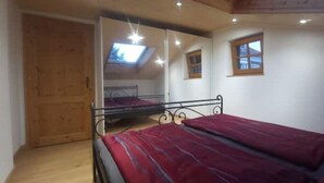 A bedroom with a bed, a wooden wardrobe, a skylight, and a small window. - Sigrid's vacation apartment Bad Tölz (Bad Tölz)