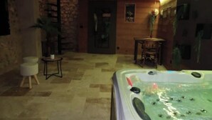 Un espace bien-être comprenant un jacuzzi, des murs en pierre et un plafond en bois.