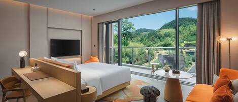 Ein modernes Hotelzimmer mit einem großen Bett, einem Schreibtisch, einem Stuhl, einer Couch und einem Balkon mit Blick auf den Wald.