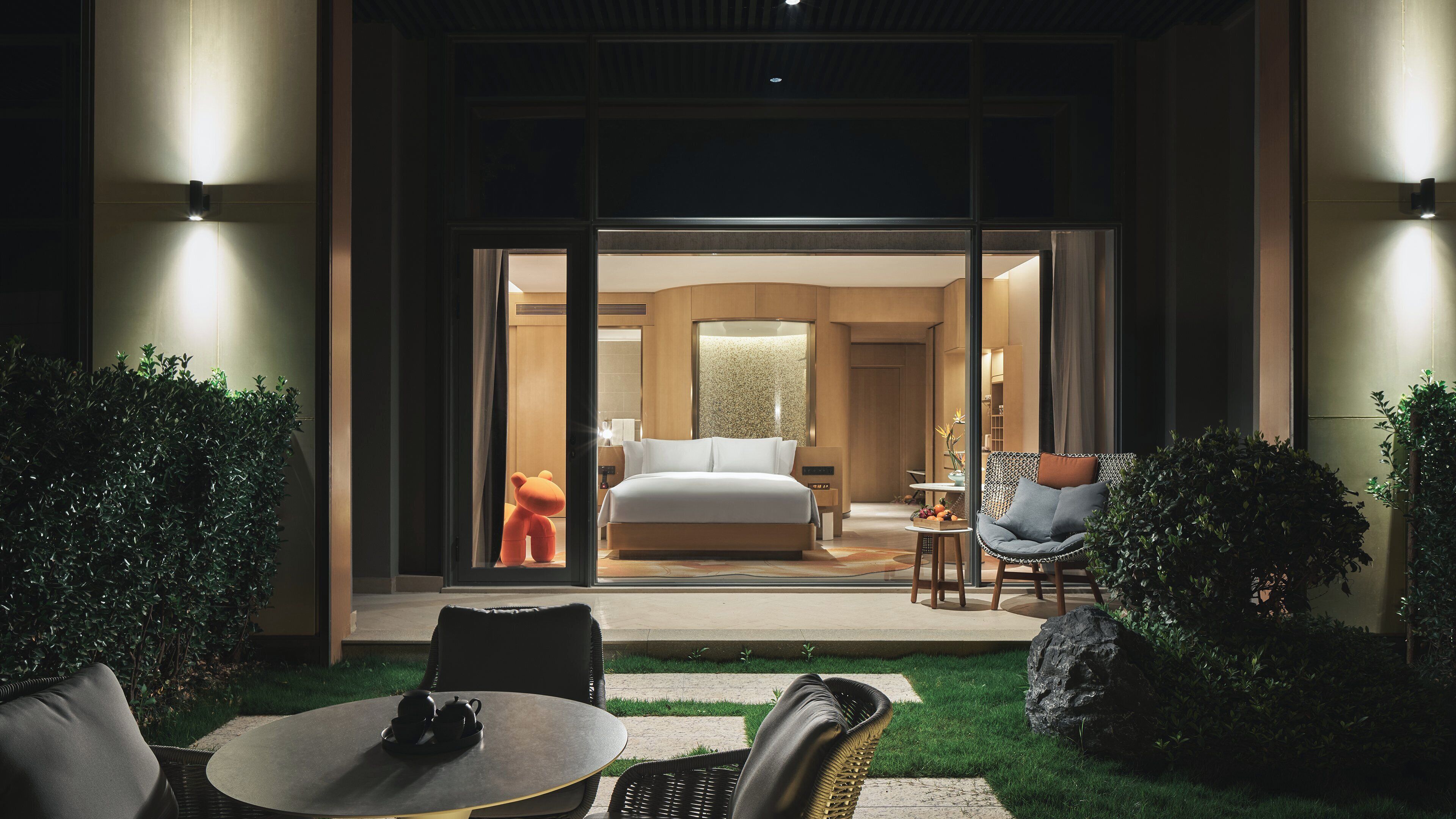 Une chambre d’hôtel moderne dotée d’un grand lit, d’un coin salon avec un canapé et une table, et offrant une vue sur la pièce grâce à une porte vitrée.