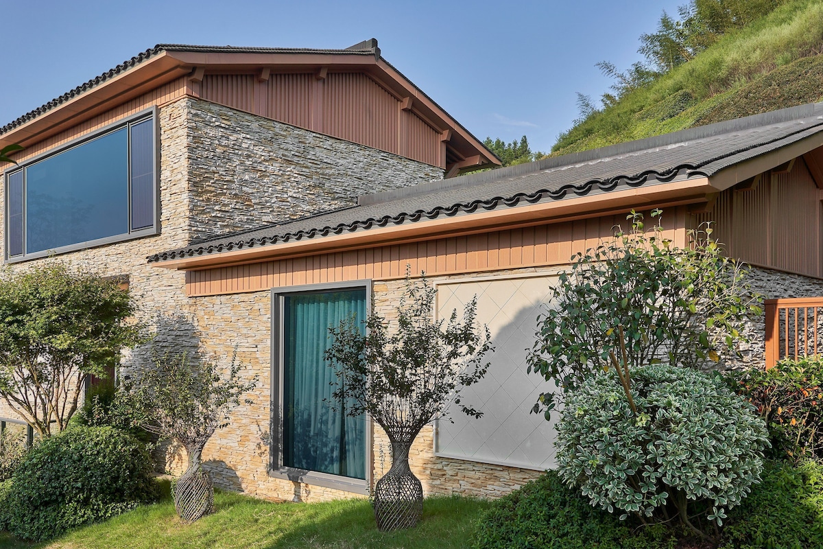 Une maison moderne à deux étages, avec une façade en pierre et en bois, de grandes fenêtres et un jardin bien entretenu.