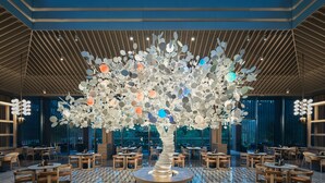 A modern interior with a unique tree sculpture centerpiece, wooden tables, and chairs arranged around it. - Hotel Indigo Hangzhou Tianmushan by IHG (Hangzhou)