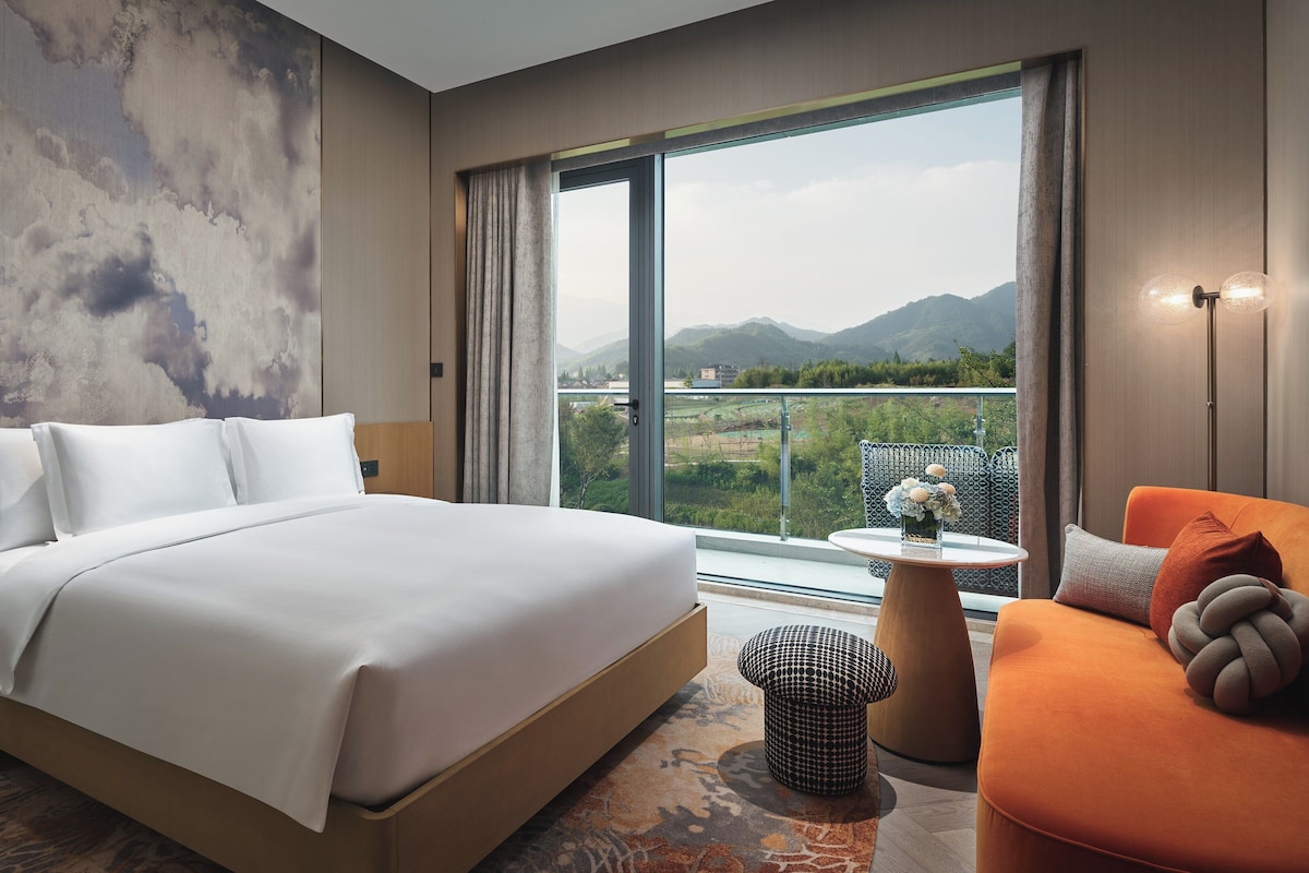 Une chambre d’hôtel moderne dotée d’un grand lit, d’un coin salon avec vue et d’un balcon offrant une vue sur les montagnes.