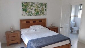 A bedroom with a wooden bed, white bedding, a blue throw blanket, a nightstand with a lamp, and a wall-mounted picture. -  3 bed 3 bath villa on the west coast (Saint James)