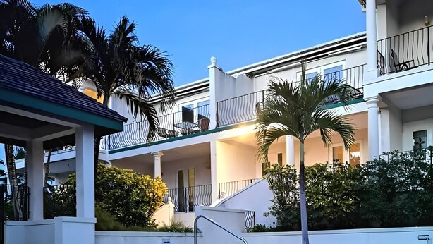 A swimming pool with a clear blue water surface, surrounded by a white building with balconies and palm trees. -  3 bed 3 bath villa on the west coast (Saint James)