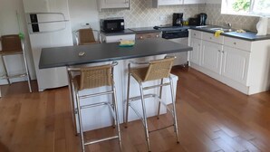 A modern kitchen with white cabinets, a central island with two bar stools, a microwave, a coffee maker, and a refrigerator. -  3 bed 3 bath villa on the west coast (Saint James)