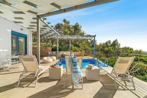 Un espace aménagé au bord de la piscine, avec des chaises longues, une pergola et une vue sur la piscine et la verdure.